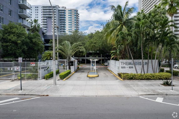 Front view of a multi-story residential building with a gated entrance and surrounding greenery.
