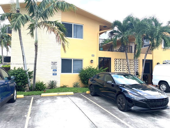 Outdoor view of a parking area in front of a two-story residential building with palm trees.