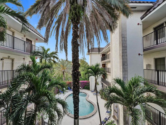 Swimming pool area with palm trees and multi-story residential buildings surrounding it.