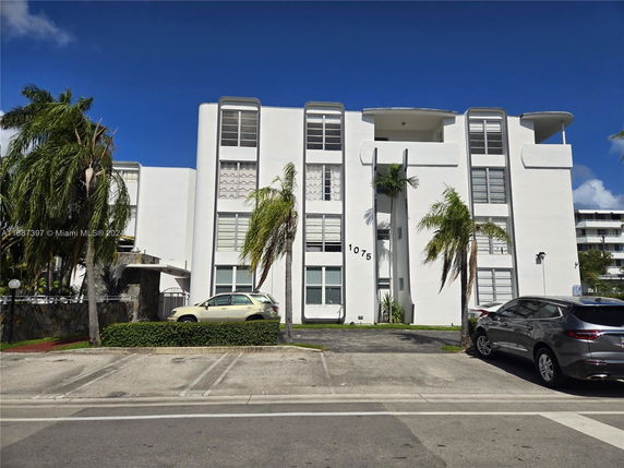 Front view of a multi-story building with a modern design and adjacent parking area.