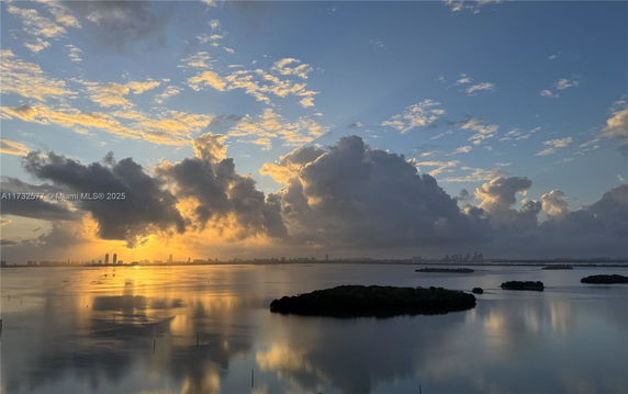 Wide angle view of a sunset over a body of water with islands and distant city skyline.