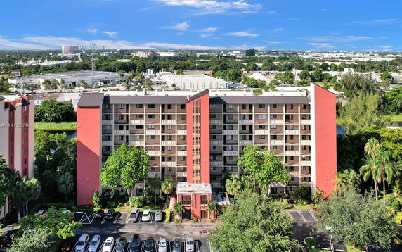 Front view of a multi-story apartment building with balconies and a parking area in front.