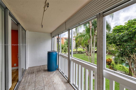 View from a balcony with a blue barrel, overlooking trees and neighboring buildings.