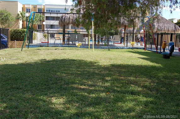 Outdoor play area with swings and grass, adjacent to a fenced swimming pool.