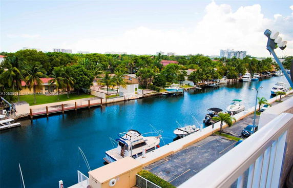 View from a balcony overlooking a waterway with boats docked alongside and residential buildings in the background.