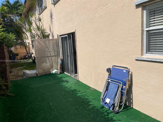 Side view of a house with beige exterior walls and a sliding glass door leading to an outdoor area with artificial grass.