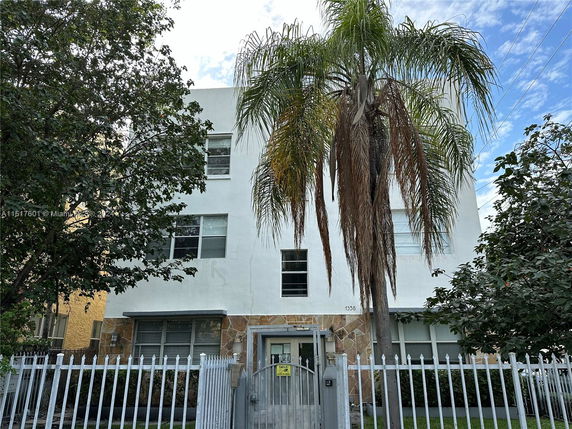 Front view of a three-story white building with metal fencing.
