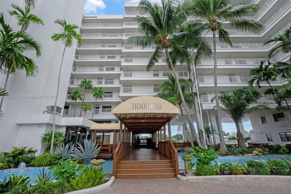 Front view of a multi-story building with a covered entrance walkway and surrounding palm trees.