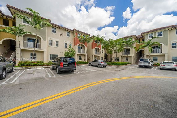View of an outdoor parking area in front of a multi-story building with palm trees.