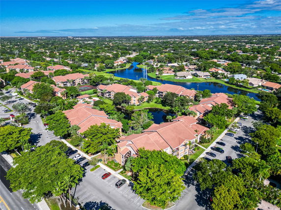 Aerial view of a residential area with multiple buildings, roads, parking areas, and surrounding greenery.