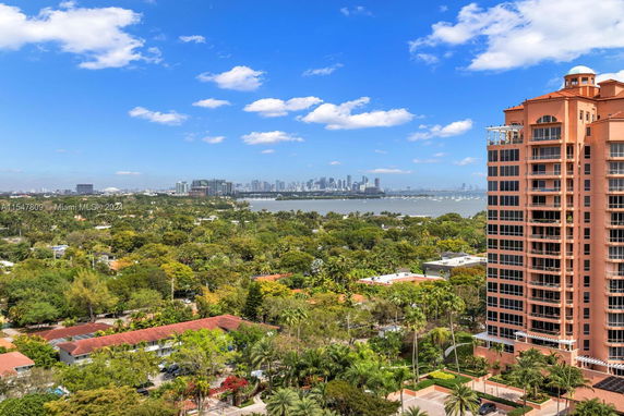 High-rise building overlooking a lush green area with a distant city skyline and water body.