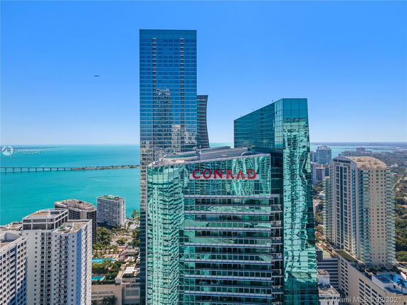 Elevated view of a tall building with 'Conrad' signage and surrounding cityscape, overlooking a body of water.