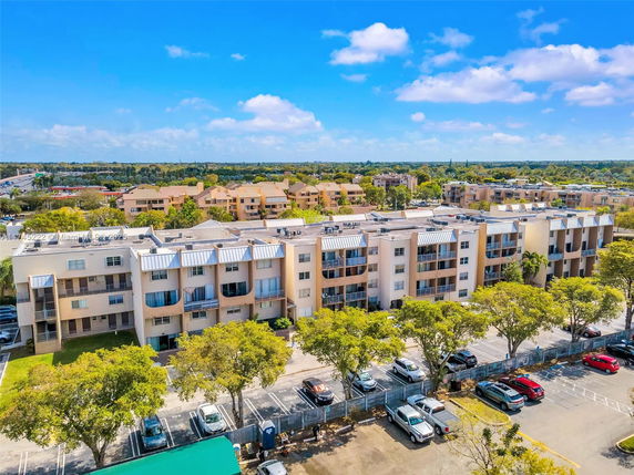 Aerial view of a multi-story residential building with parking spaces and surrounding neighborhood.