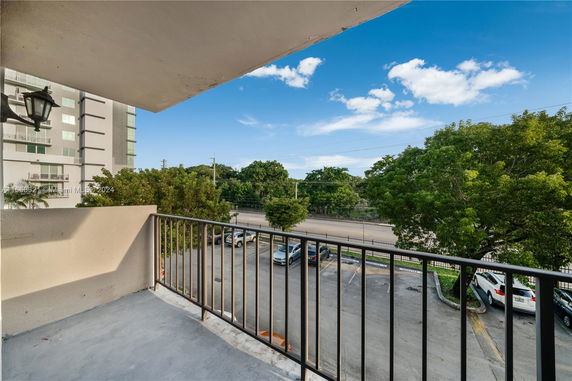 View from a balcony overlooking a parking area and trees.