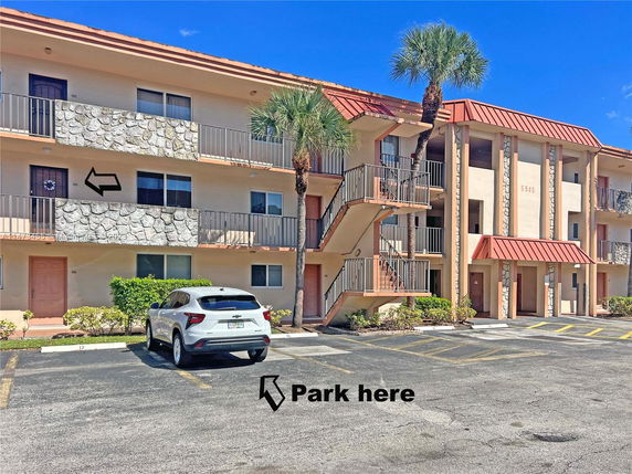 Front view of a multi-story apartment building with external staircases and parking area.