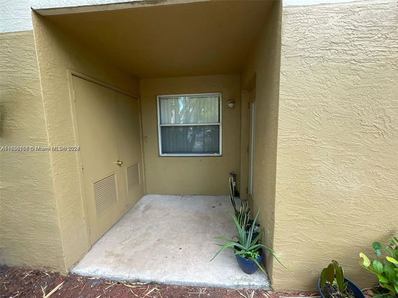 Front view of a small outdoor entryway with a window and door, surrounded by beige walls.