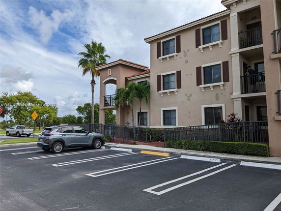 Front view of a three-story residential building with balconies and parking spaces.