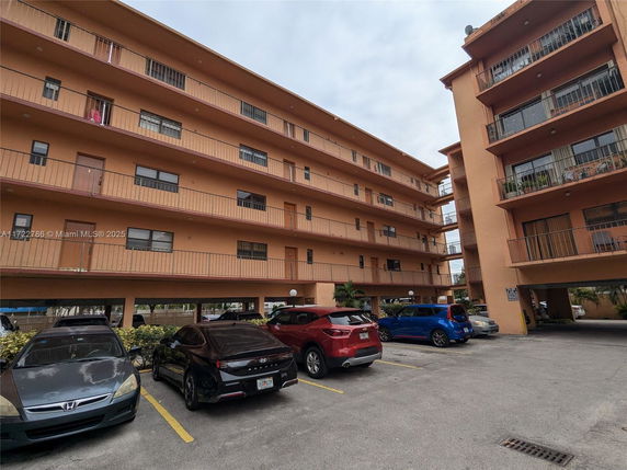 Multi-story residential building with multiple balconies and a parking area in front.
