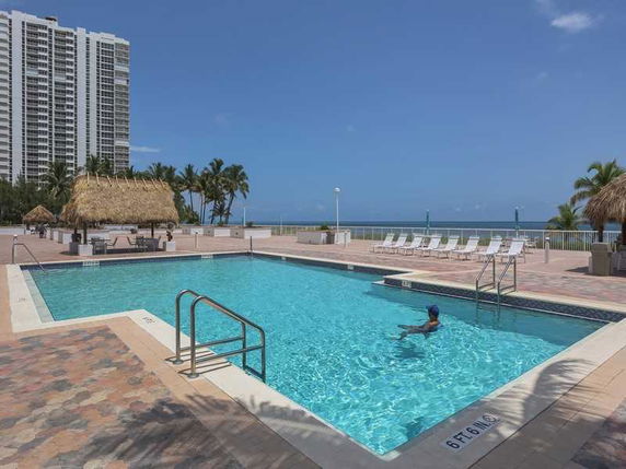 View of a swimming pool area with high-rise buildings and oceanside loungers.