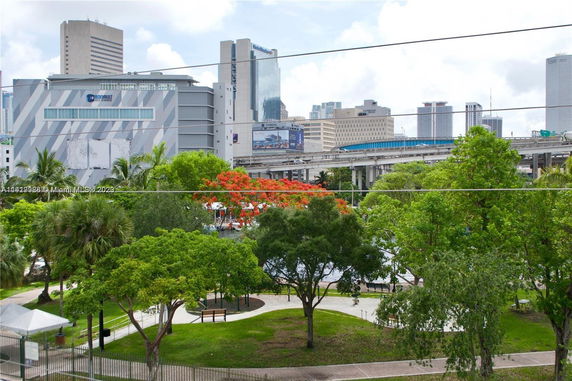 View of a cityscape with buildings and elevated road seen through a park with trees.
