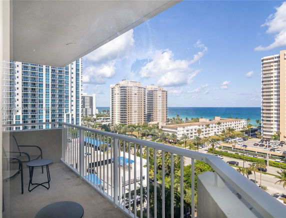 Panoramic view of high-rise buildings and ocean from a balcony.