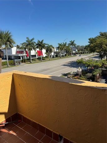 View from a balcony overlooking a street lined with palm trees and commercial buildings.