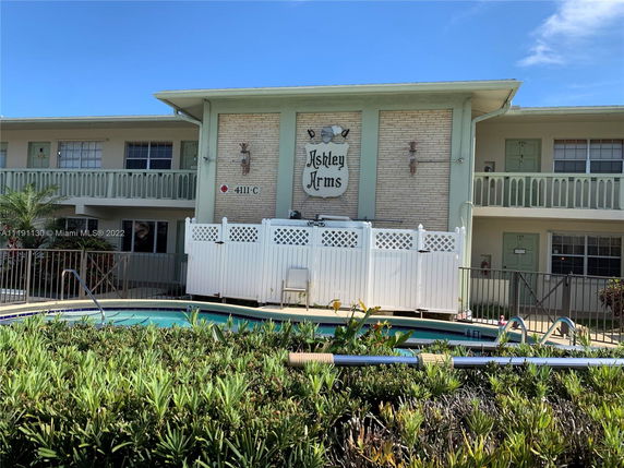 Front view of a two-story building with balconies and a swimming pool in the foreground.