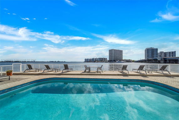 Outdoor swimming pool with lounge chairs overlooking the water and city skyline.