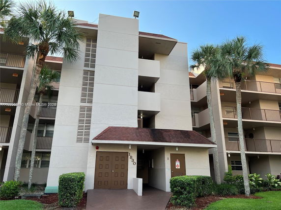Front view of a multi-story apartment building with balconies and palm trees.