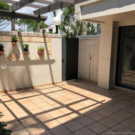 Outdoor patio area with tiled floor, pergola, and potted plants on the wall.