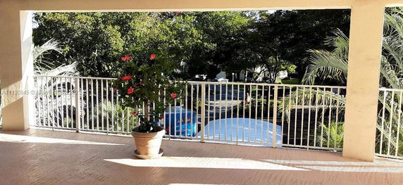 Balcony view overlooking a green area with trees and potted plants.