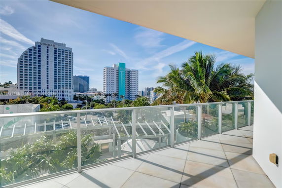 Panoramic view from a balcony showing city buildings and palm trees.