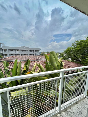 View from a balcony overlooking rooftops with a cloudy sky and surrounding greenery.