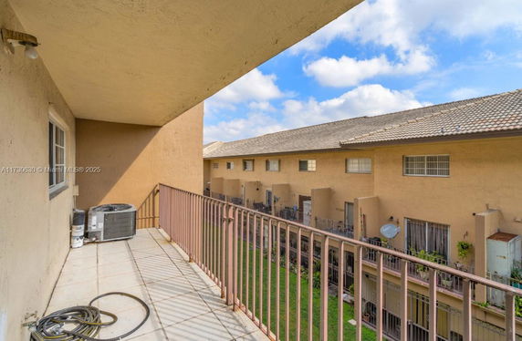 A rooftop area with an air conditioning unit and railing, adjacent to a building with tiled roofing.