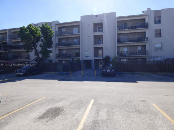 Front view of a multi-story residential building with balconies and a parking area in front.
