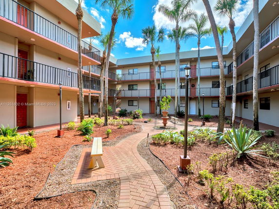 View of a multi-level residential building with balconies surrounding a landscaped courtyard with plants and a walking path.