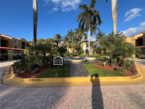 Front view of a multi-story residential building with palm trees and a water fountain in the foreground.