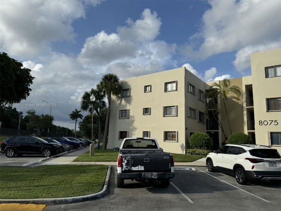 Front view of a multi-story beige apartment building with parking area.