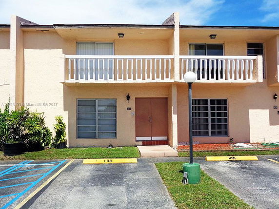 Front view of a two-story building with a balcony and parking area.