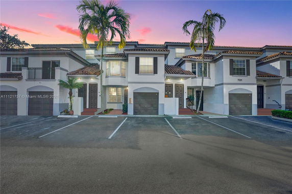 Front view of a two-story townhouse with a garage and palm trees.