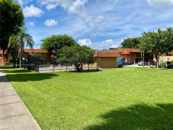 View of a grassy area with buildings and parked cars in the background.