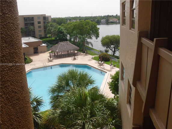 View of a swimming pool area with surrounding buildings and a water body in the background.