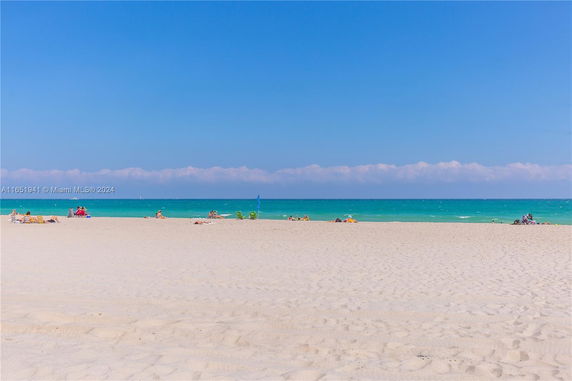 Sandy beach with people relaxing under a clear blue sky and calm ocean.