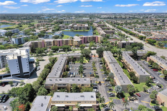 Aerial view of a residential area with several multi-story buildings, parking lots, and nearby roads.