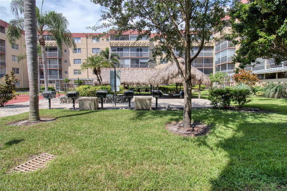 View of apartment complex with grass, trees, and outdoor grilling area.