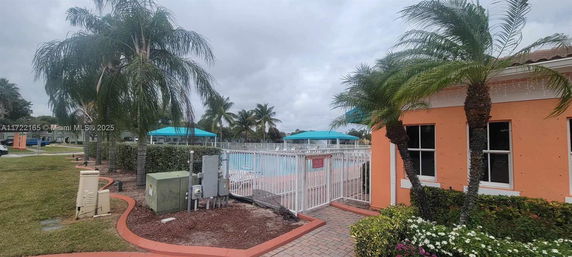 Outdoor swimming pool area with palm trees and a nearby building.