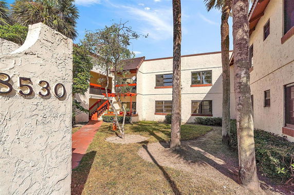Front view of a two-story apartment building with outdoor stairs and surrounding greenery.