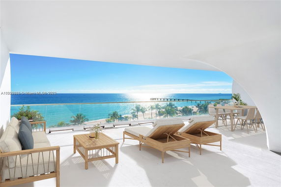 Panoramic view from a patio with outdoor furniture overlooking the ocean and beach.