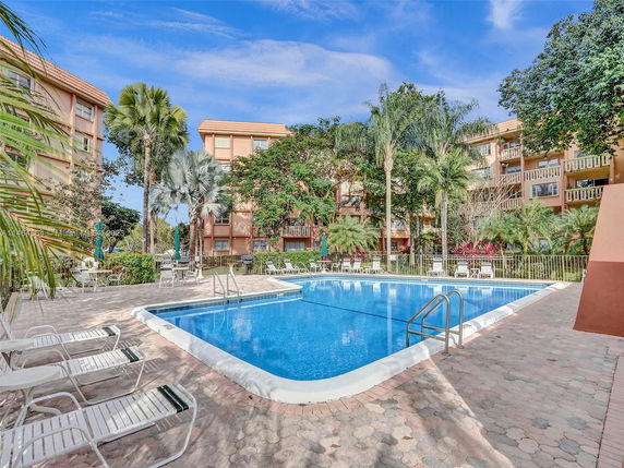 Outdoor swimming pool surrounded by multi-story residential buildings and palm trees.