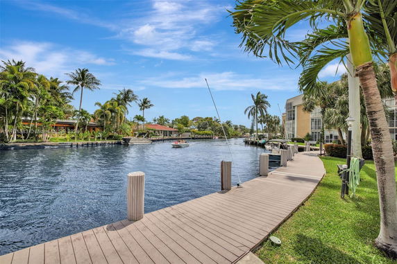 View of a waterfront area with a dock and surrounding palm trees, buildings, and boats on a canal.